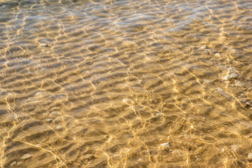 Fototapeta na wymiar Patterns of the sun shining through the crystal clear water and the sand wave formations with scattered white rocks near the shore of the Mediterranean Sea in Israel. 