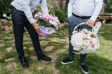 Two gay men with baskets, bouquets of flowers stand in the park on a holiday. Photography, love, lgbt, wedding.
