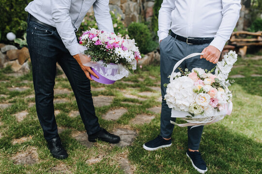 Two gay men with baskets, bouquets of flowers stand in the park on a holiday. Photography, love, lgbt, wedding.
