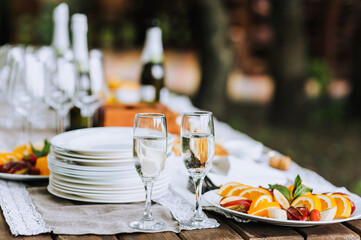 A round plate with a variety of fruits, champagne glasses, empty dishes stand on a wooden table at a banquet. Photo of food, dessert, buffet at the holiday.