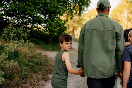 Portrait of boy holding hand of counselor while walking on footpath at summer camp