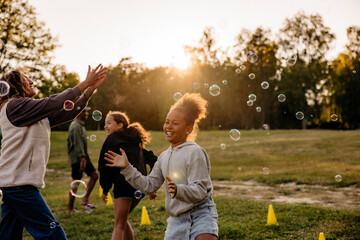 Girl playing amidst bubbles with friends in playground at summer camp
