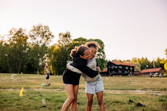 Happy female friends embracing each other while standing on grass in playground