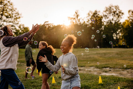 Girl playing amidst bubbles with friends in playground at summer camp