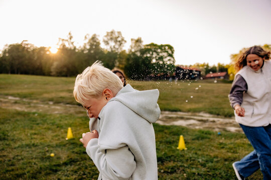 Side view of blond boy avoiding friends splashing water while playing in playground