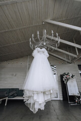 Fototapeta na wymiar Beautiful white long lace wedding dress of the bride hangs on a chandelier in the house outdoors.