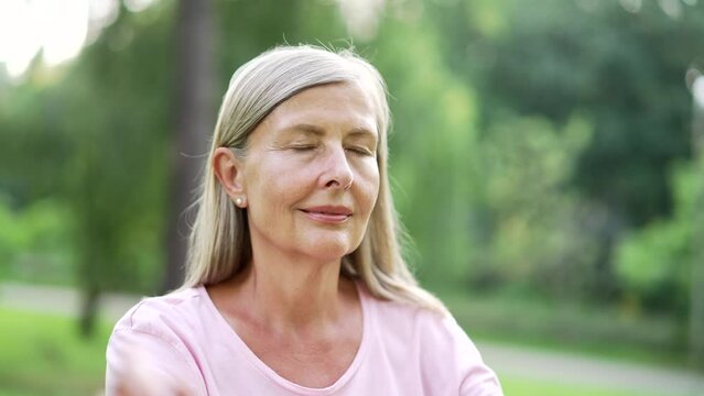 Close Up. Senior Adult Active Gray Haired Woman Meditating While Sitting In An Urban City Park. Mature Old Fitness Female Doing Yoga Outside. The Pensioner Relaxes With Eyes Closed In Forest In Nature