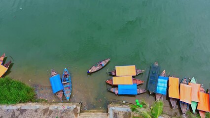 Drone shot with an angle down the river with a boat anchored and a ferryman rowing the boat to take people across the river to go to the market in the ancient town of Hoi An, Vietnam.