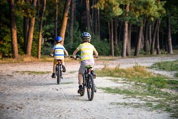 Family in the park on bicycles. two sibling brothers kids boys compete in riding. view from back