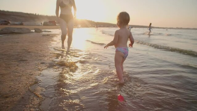 Toddler running on a coastline, family vacation with child. Summer leisure activity on the seaside, slow motion. Healthy lifestyle theme for a family