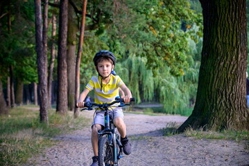 Portrait of happy toddler child boy riding on bike with helmet. He rides from a small hill, through a sandy forest path. Sport concept: kids ride bicycle first bike active toddler kid