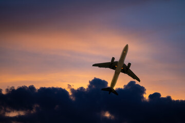Silhouette airplane commercial trip or cargo flying above dark cloud with twilight sun sky background.