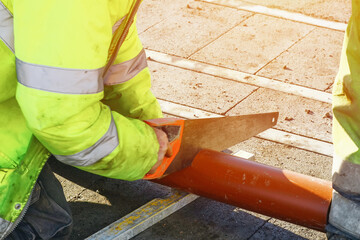 Builder cutting plastic pipe with hand saw during new house internal and external drainage system construction