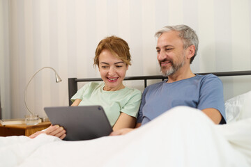 Smiling mature couple using digital tablet at home in bed