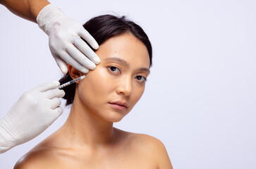 Hands of beautician in white surgical gloves injecting botox in cheek of asian woman, copy space - obrazy, fototapety, plakaty