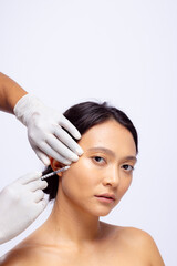 Obraz na płótnie Canvas Hands of beautician in white surgical gloves injecting botox in cheek of asian woman, copy space