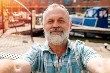 a bearded retirement walking on the quays, pier, sitting on bench, taking selfie, having video chat, looking at yacht, sailboat, boat. Lifestyle concept
