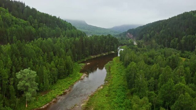 Aerial view of beautiful river flowing among green forest. Ural mountains landscape