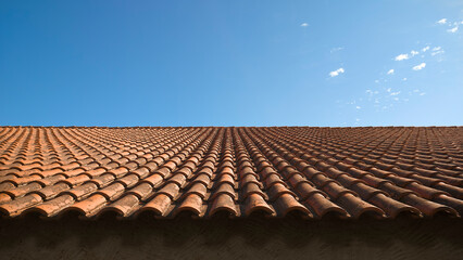 Weathered red tile roof with side sunlight on a blue sky background