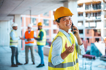 Construction woman closing deal on the phone. Portrait of civil engineer woman doing business, talking on smartphone and holding tablet computer in hand, standing against high buildings 
