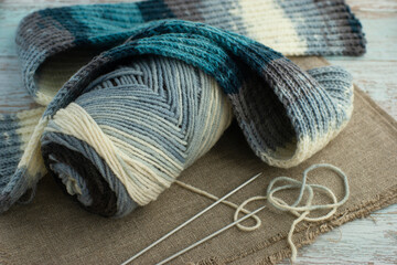 Yarn for knitting and scarf. The scarf is knitted from yarn in gray - blue tones. Knitting needles, scarf and yarn close-up.