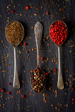 Spoons with caraway, red and mixed peppercorn on black background