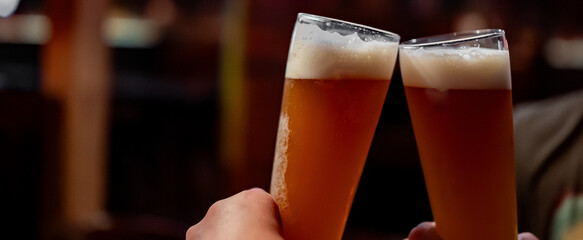 Two friends hands clinking glasses of craft beer at the pub or bar
