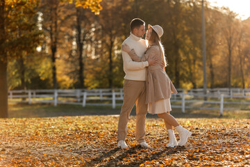 Fototapeta premium Young stylish couple lovers are hugging and kissing in the autumn park. Lovely romantic moment between man and woman in love, looking to each others. Happy family. Love, youth, happiness concept.