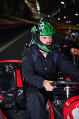 focused man in sportswear and helmet driving sport car for karting on indoor circuit, hobby