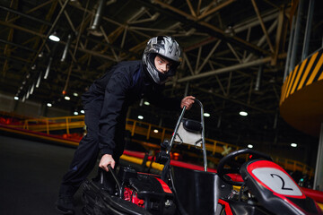 Fototapeta na wymiar motorsport and speed drive, focused kart driver in helmet and sportswear pushing go kart on circuit
