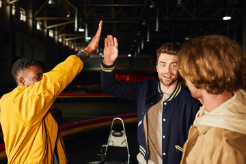 Fototapeta na wymiar happy interracial friends giving high five inside of indoor track, go-cart concept, motorsport hobby