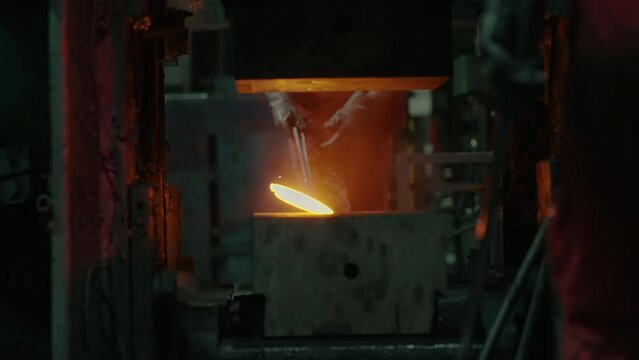 A press in an automotive products factory compresses a hot iron automotive part. Close-up slow-motion shot.