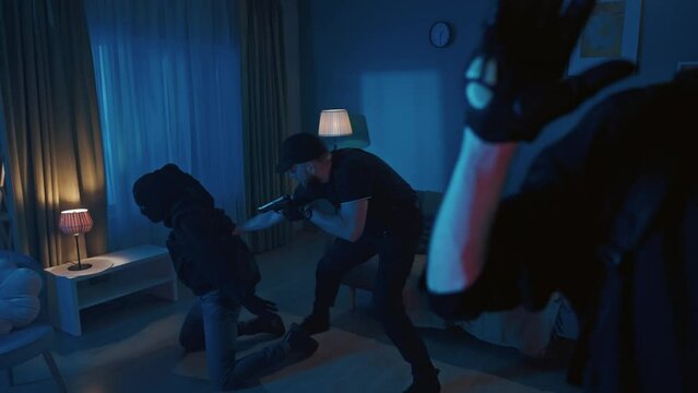 Video of two burglars, intruders, being caught red-handed in the house. Policeman is pointing a gun at them. Men get down and raise hands.
