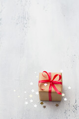 A small gift wrapped in kraft paper with a red ribbon on a light blue background, surrounded by a shiny confetti star, copy space. Christmas background, holiday background