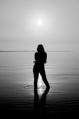 Woman's silhouette in the sea in the backlight of the sun. Black and white photo of a girl in sea...