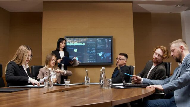 A diverse multinational team of professional business people meet in the conference room of a modern office. Creative team at the table discussing data analysis and planning a marketing campaign