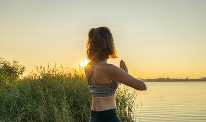 Woman near the river during warm sun rise making breathing exercises. Sun and sky in the morning, peace of nature