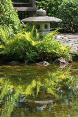 Fototapeta na wymiar stone lantern is reflected in the water of a pond in a Japanese garden