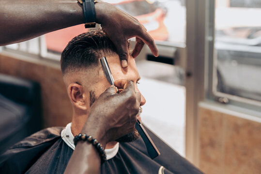 Crop barber shaving hair of client with razor