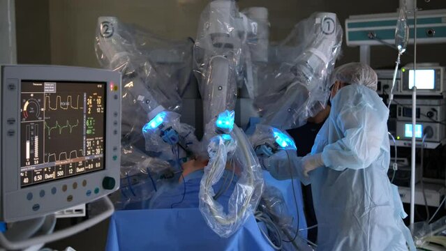 Robotic surgery in a sterile environment. A nurse supervises a multi-armed robot performing a surgical procedure. Medical equipment and monitors in the foreground.