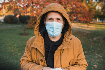 A bearded man in  stylish jacket blows his nose into a paper napkin outdoors in an autumn park. Seasonal autumn cold