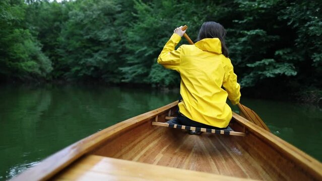 Slow motion of woman in yellow raincoat paddling canoe