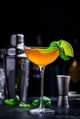 Spring grass alcoholic cocktail drink with scotch whiskey, apple liqueur, ginger, lemon juice, basil and ice, dark bar counter background