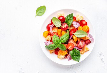 Panzanella salad with stale ciabatta bread, colorful tomatoes, red onion, olive oil, salt and green basil, white table background, top view