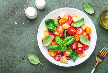 Panzanella vegetable salad with stale bread, colorful tomatoes, olive oil, sea salt and green basil, green stone table background, top view