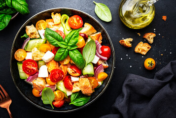 Panzanella salad with stale ciabatta bread, colorful tomatoes, soft cheese, red onion, olive oil, sea salt and green basil, black table background, top view