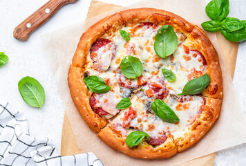 Homemade pizza with italian salami sausage, mozzarella cheese, tomato sauce and green basil on white kitchen table background, top view