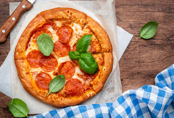 Pepperoni pizza with salami sausage, mozzarella cheese, spicy tomato sauce and green basil leaves, rustic wooden background, top view