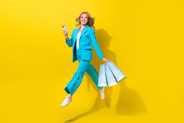 Full size photo of attractive girl dressed blue formalwear hold new clothes smartphone make online order isolated on yellow background