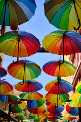Fototapeta na wymiar Lots of rainbow-colored umbrellas hanging above street. Decoration of streets made of umbrellas